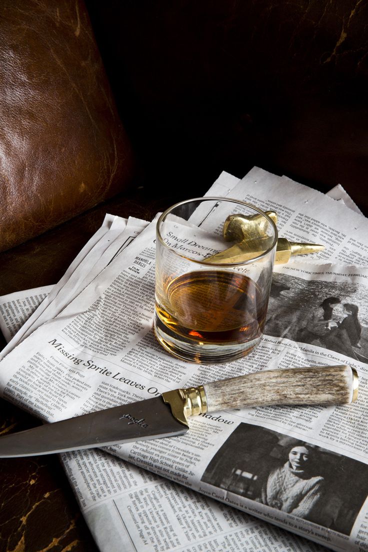 a glass cup filled with tea sitting on top of newspaper next to a knife and spoon