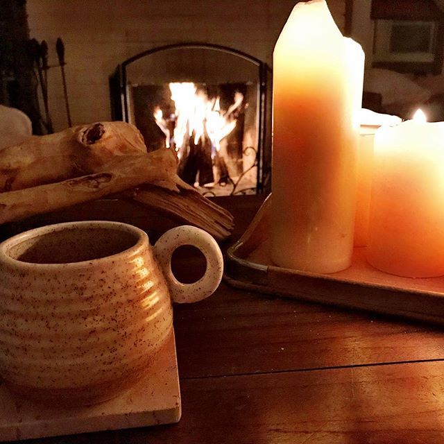 some candles are sitting on a table next to a fire place and a tray with two mugs