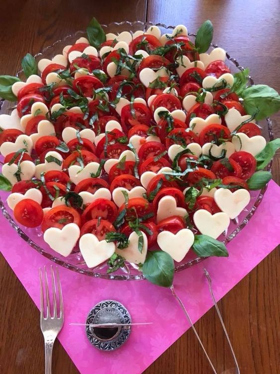 a platter filled with tomatoes and hearts on top of a pink napkin next to utensils