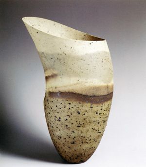 a white and brown vase with black speckles on the bottom is shown in front of a gray background