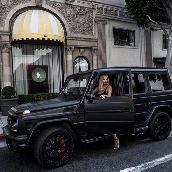 a woman is sitting in the driver's seat of a black mercedes g class