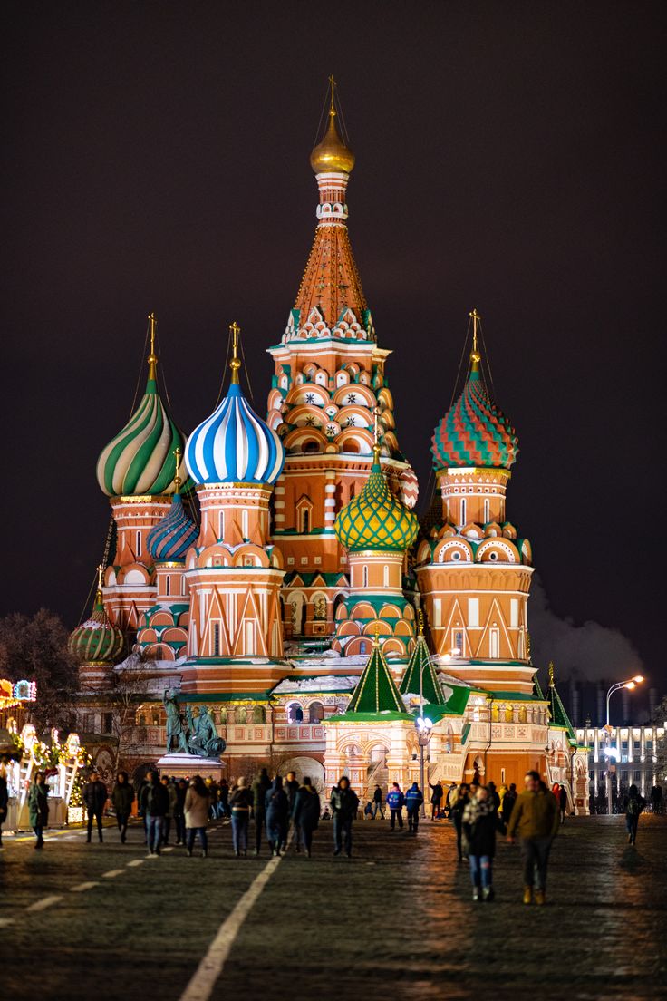 many people are walking around in front of an ornate building with domes on it at night