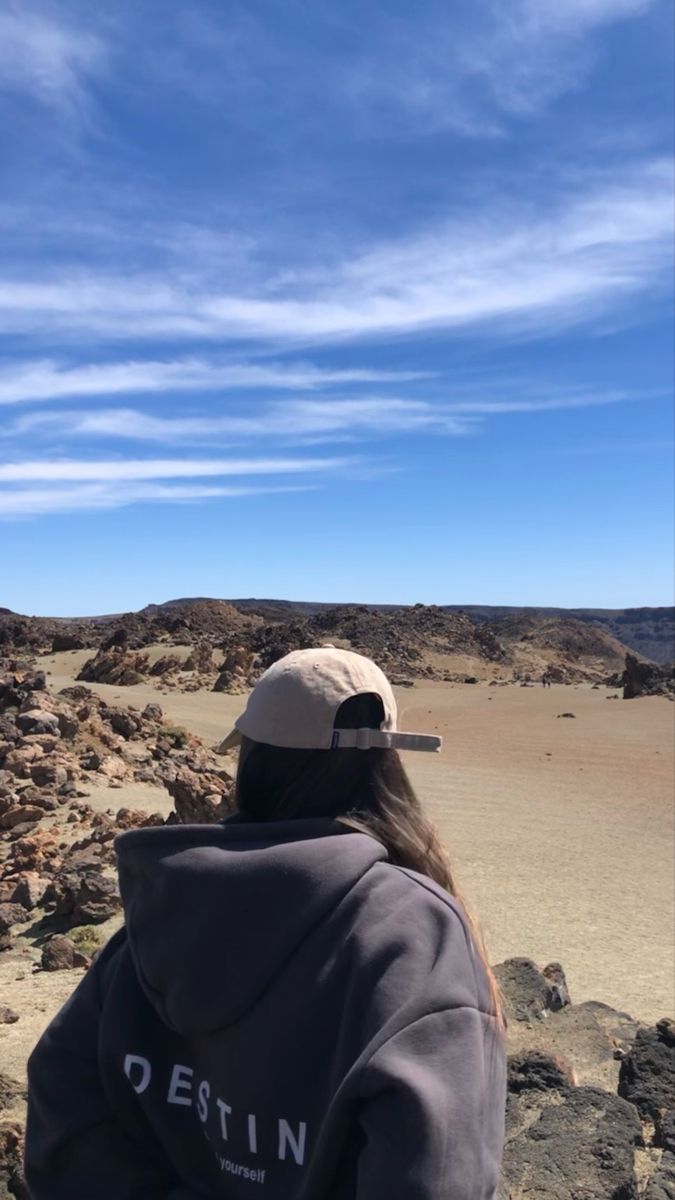 a person sitting on rocks looking out at the desert and blue sky with wispy clouds