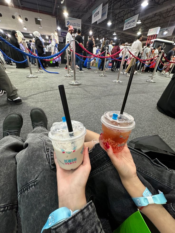 two people holding drinks in their hands while sitting on the floor at an indoor event