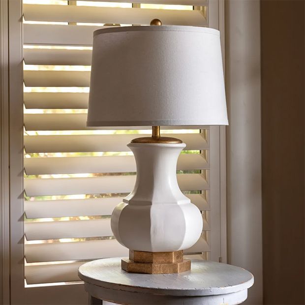 a white lamp sitting on top of a table next to a window covered in blinds