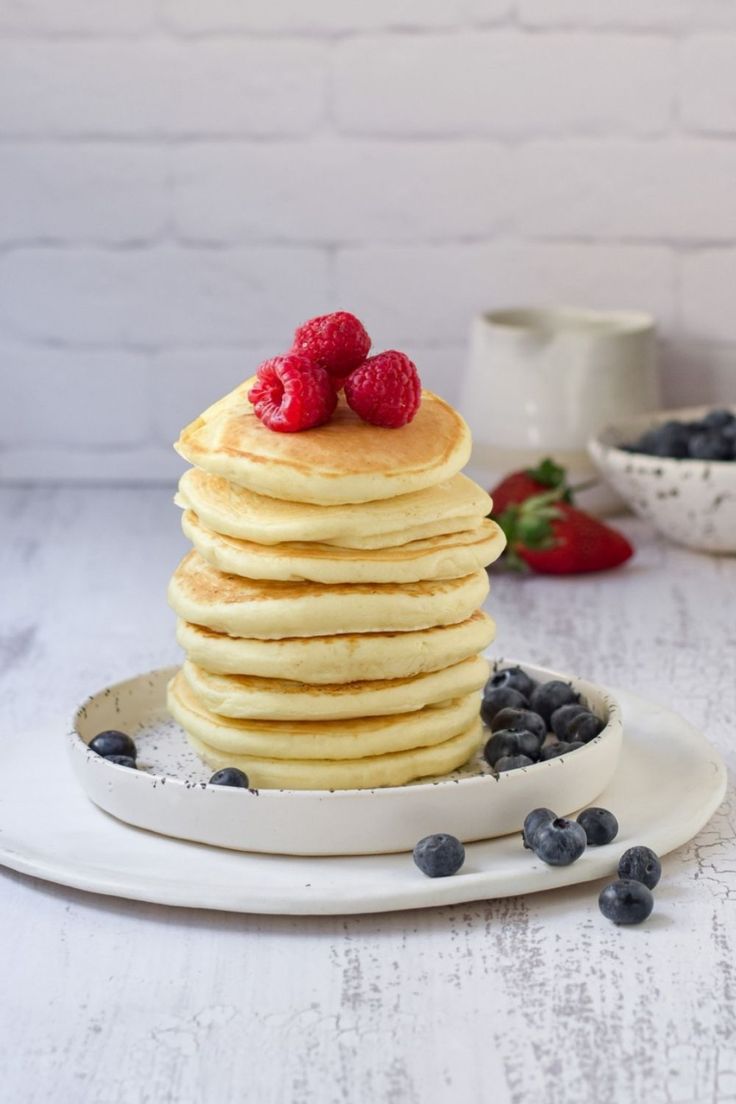 a stack of pancakes topped with raspberries and blueberries on a white plate