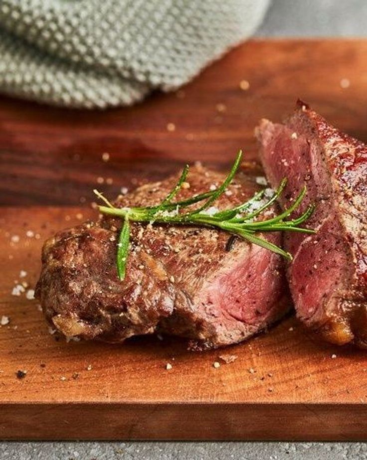 two pieces of steak sitting on top of a wooden cutting board