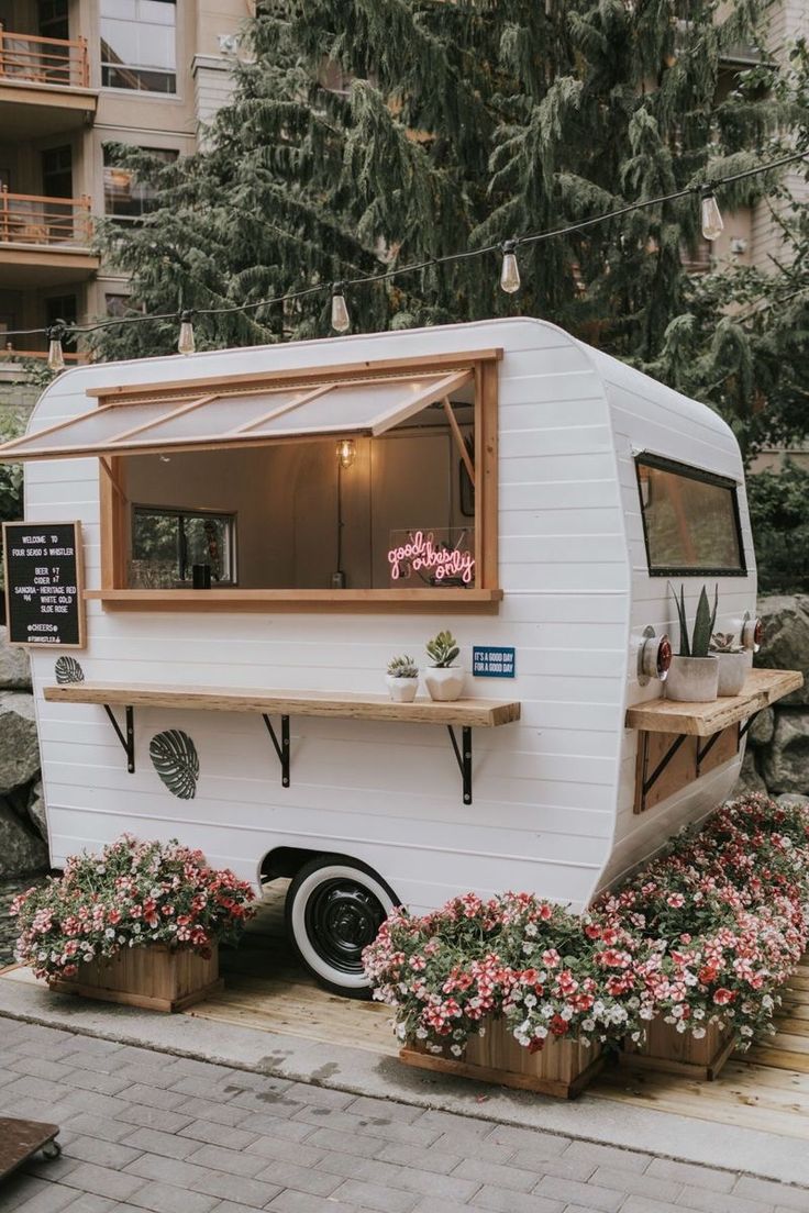 a food truck parked on the side of a road with potted plants in front of it