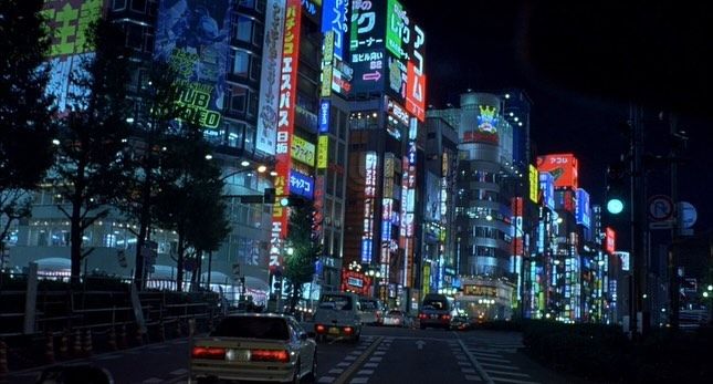 a city street filled with lots of tall buildings and neon signs on the side of it