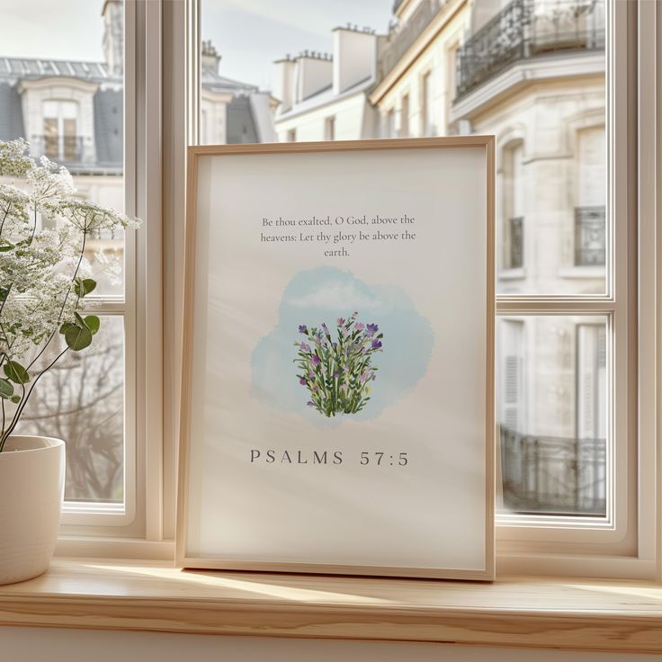 a white vase with flowers sitting on top of a window sill next to a framed poster