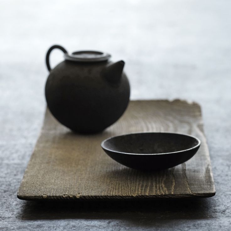 a black tea pot sitting on top of a table next to a bowl