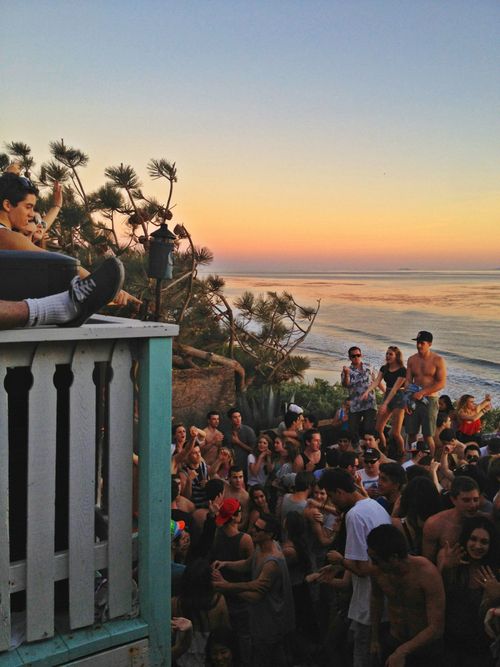 a group of people standing on top of a balcony next to the ocean at sunset