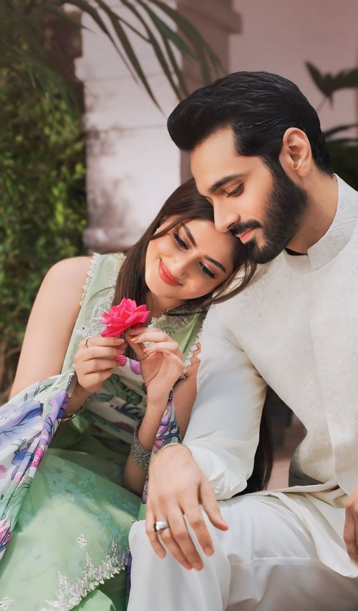 a man and woman sitting next to each other on a bench holding a flower in their hands