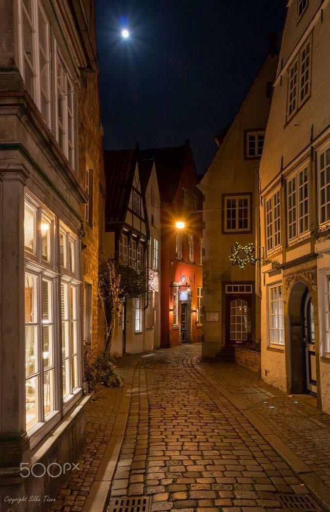 an empty cobblestone street at night with the moon in the sky