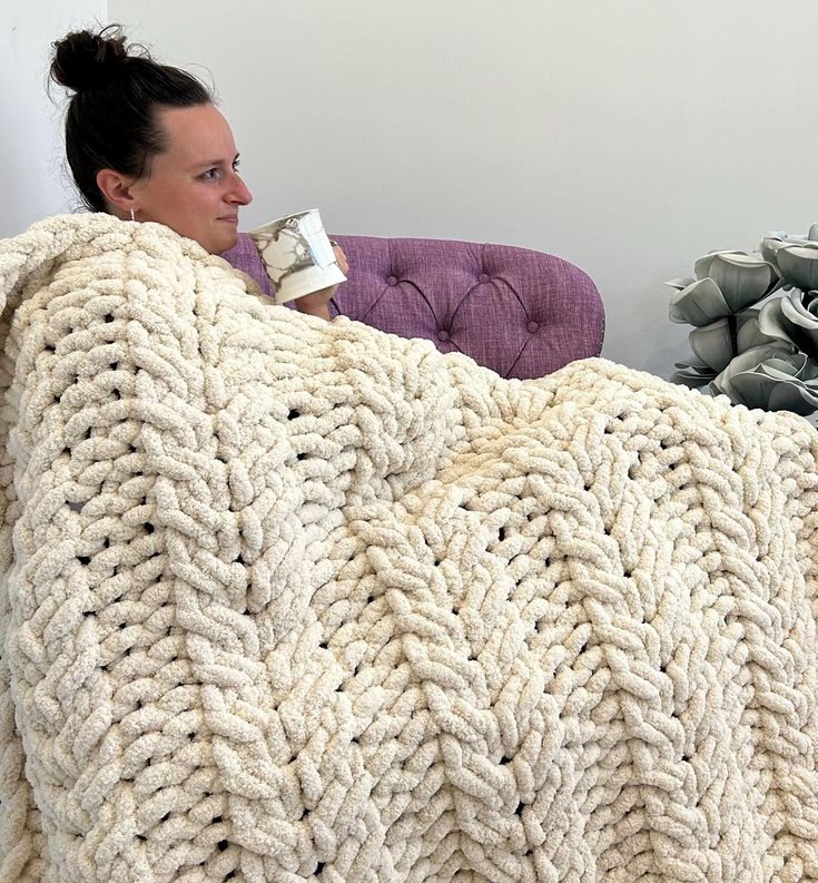 a woman sitting on a couch holding a coffee cup in her hand while wrapped in a blanket