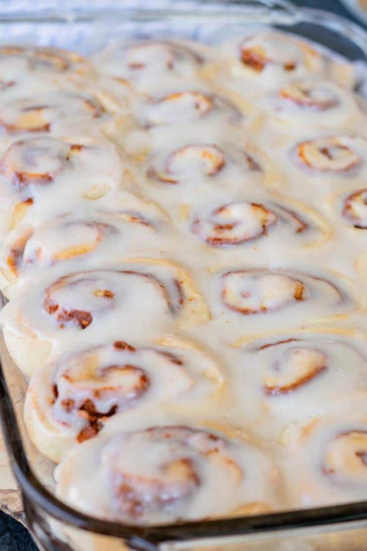 a pan filled with cinnamon rolls covered in icing on top of a wooden table