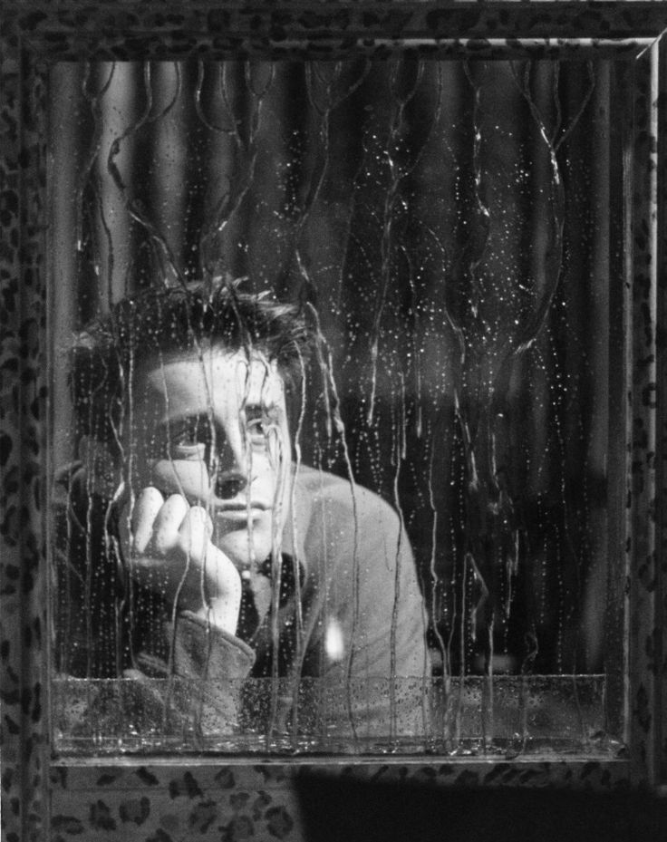 black and white photograph of a man looking out the window with his hand on his face