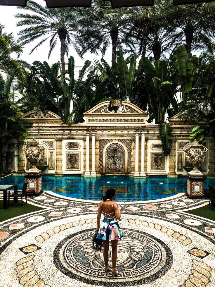 a woman standing in front of a pool surrounded by palm trees and other greenery