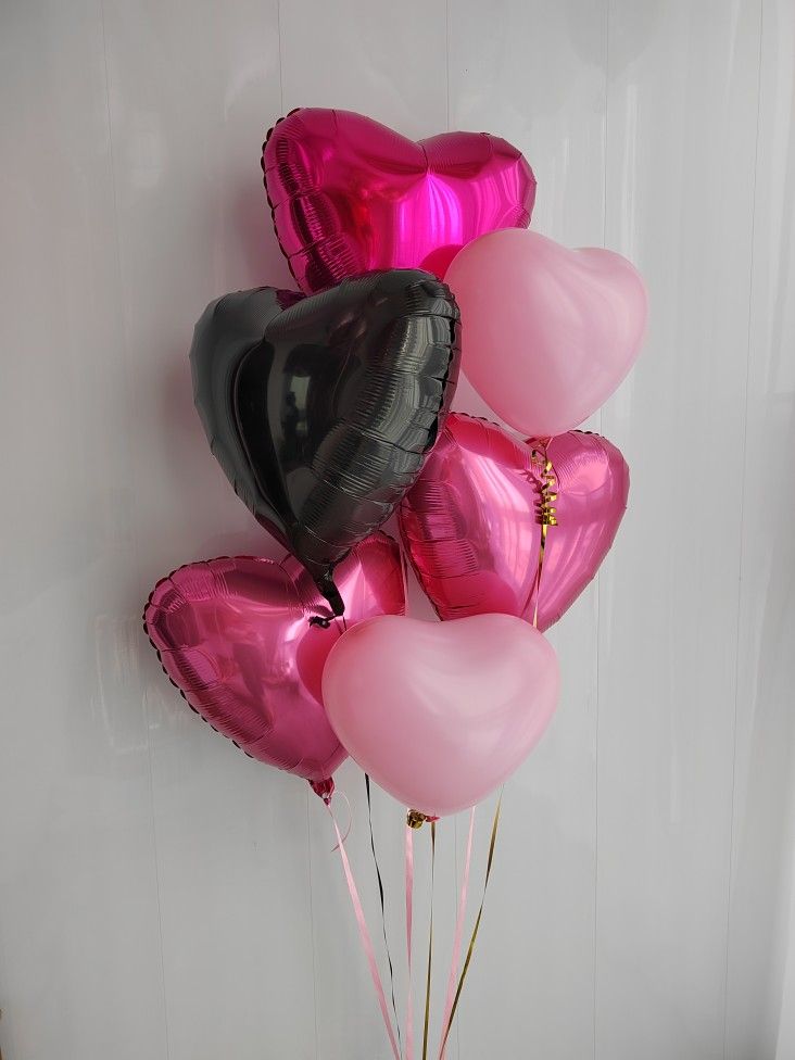 pink and black heart shaped balloons in a vase on a table next to a white wall