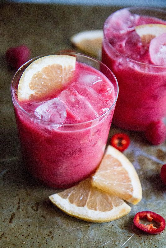 two glasses filled with fruit and ice on top of a counter next to sliced lemons