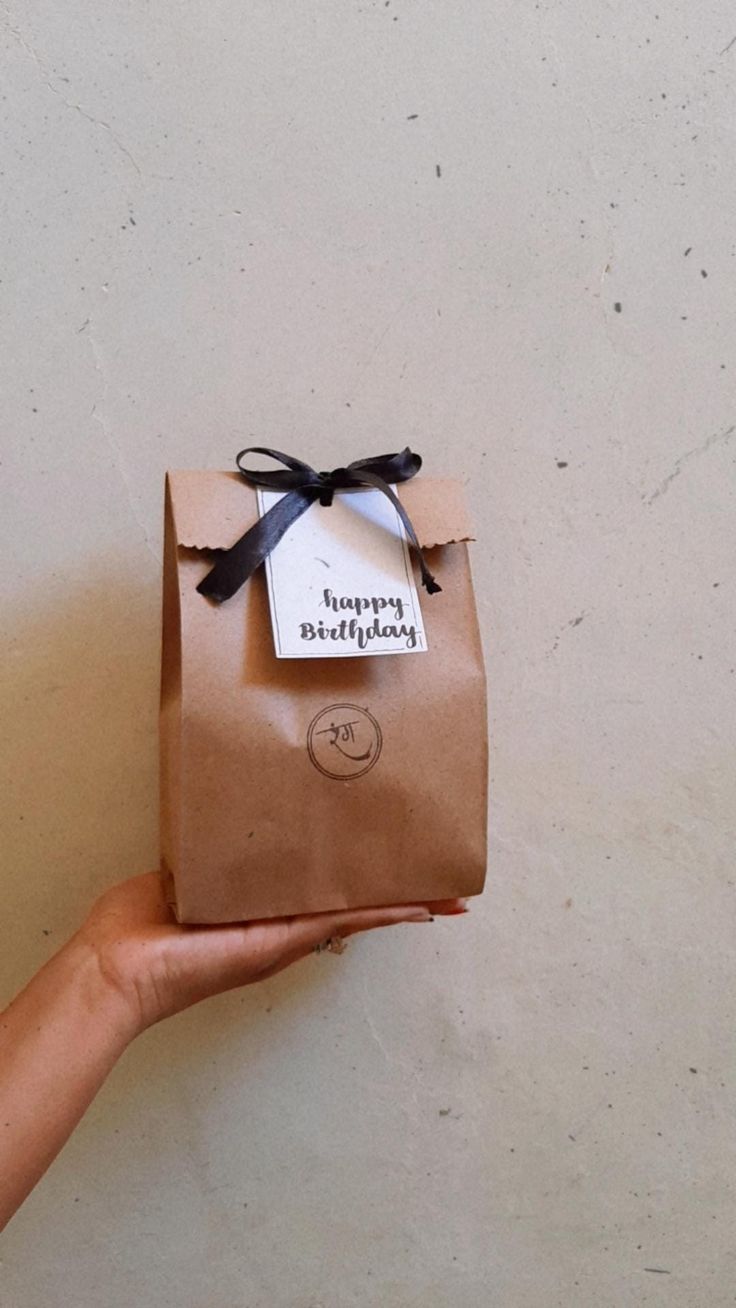 a hand holding a brown paper bag with a tag on it that says happy birthday