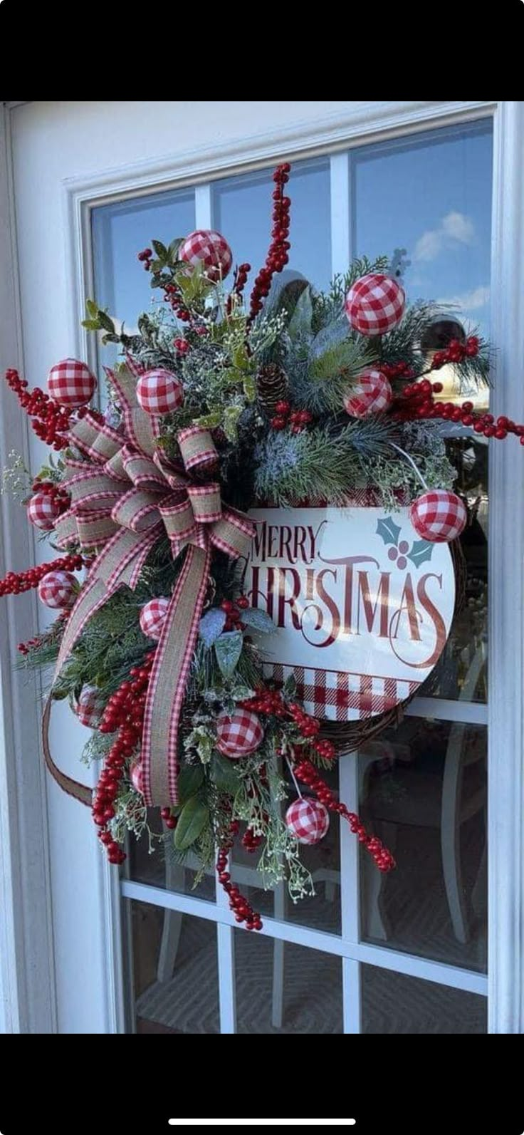 a christmas wreath is hanging on the front door with red and white plaid ribbon around it