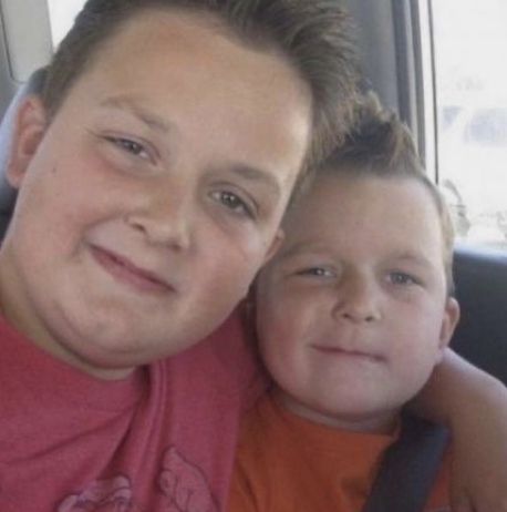 two young boys sitting in the back seat of a car, one with his arm around the other's shoulder