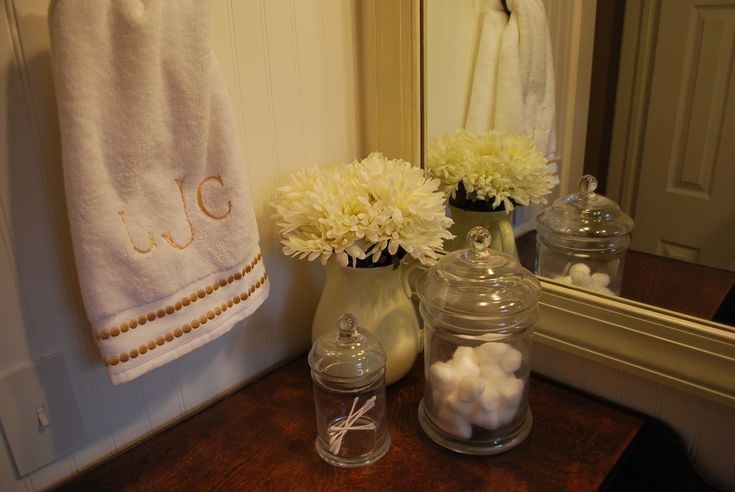 a bathroom sink with flowers and towels on the rack next to it, along with two glass jars filled with cotton balls