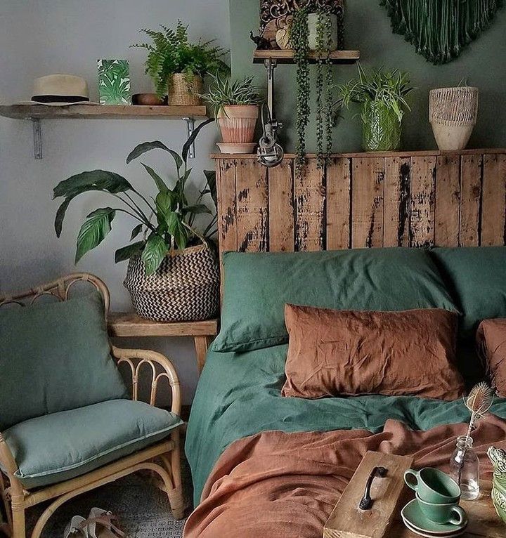 a bed with green sheets and pillows in a room filled with potted plants on the wall