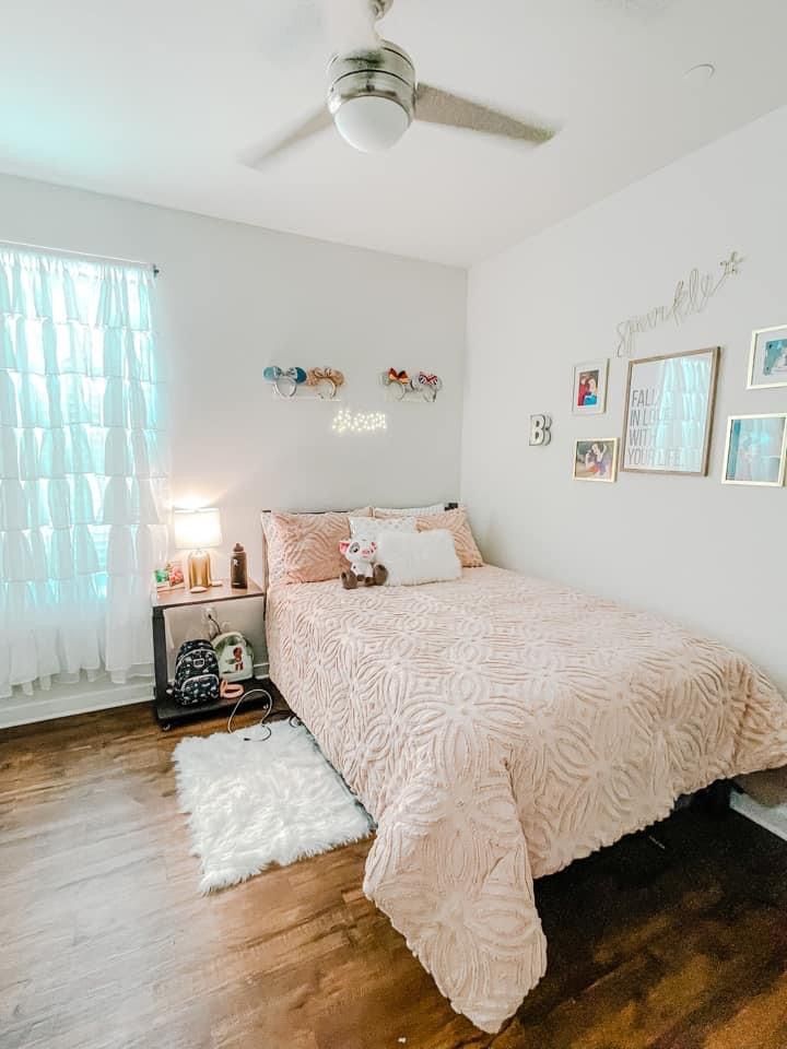 a bedroom with white walls and wood flooring has a pink comforter on the bed