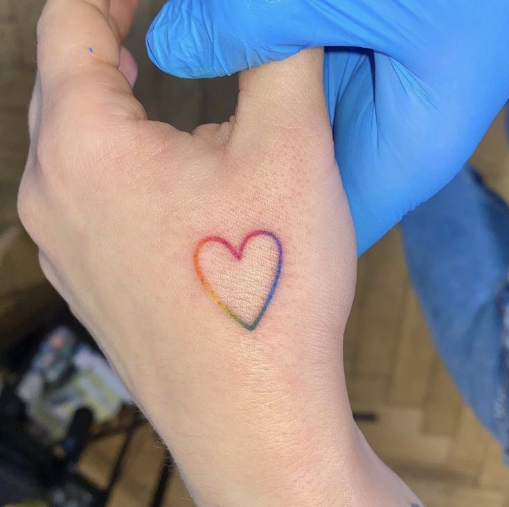 a person with a heart tattoo on their left hand and blue glove holding the wrist