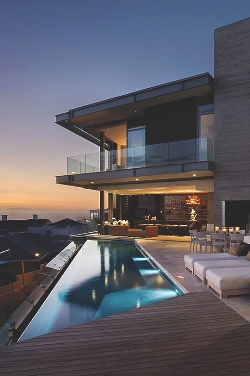 an outdoor swimming pool next to a large house with glass balconies on the roof