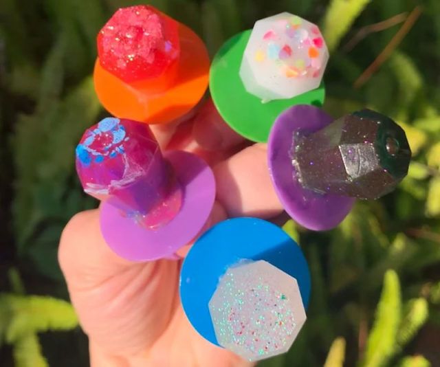 a person holding five different colored rocks in their hand with plants in the back ground