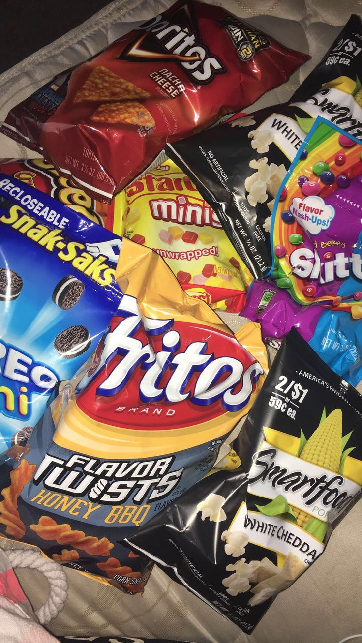 a pile of snacks sitting on top of a bed next to a bag of chips