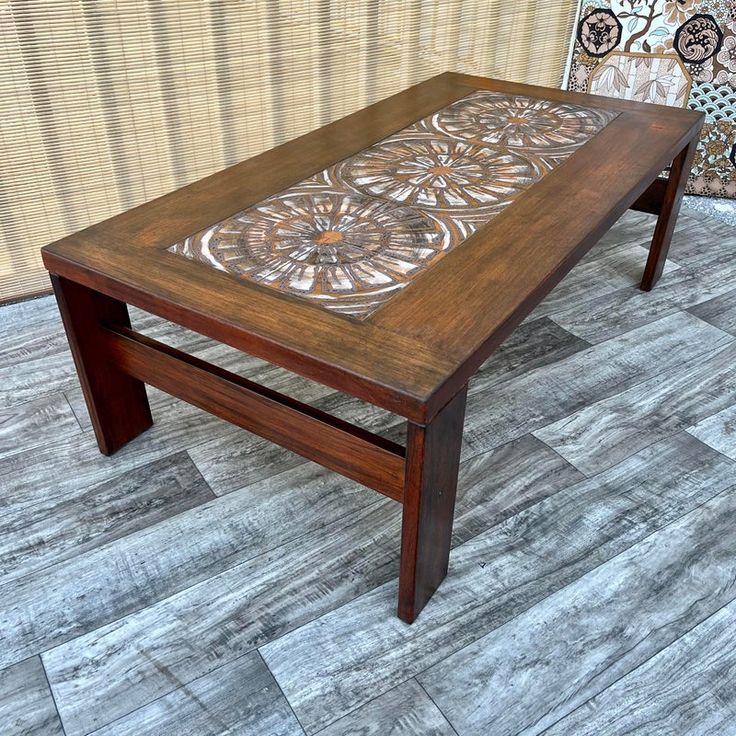 a wooden table sitting on top of a tile floor next to a wall with an intricate design