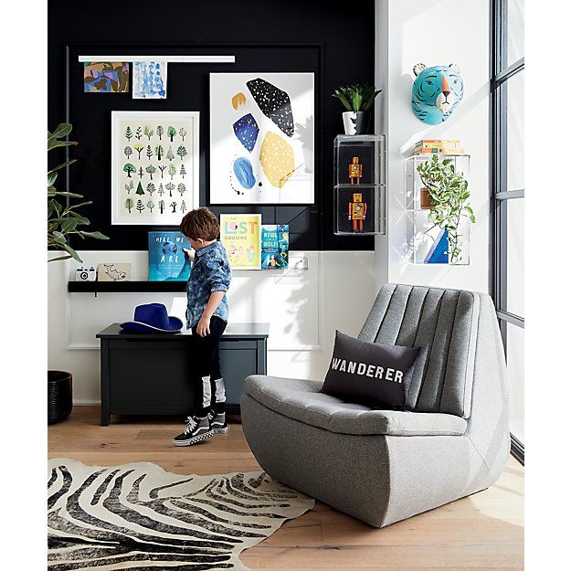 a young boy standing in front of a chair next to a wall with pictures on it