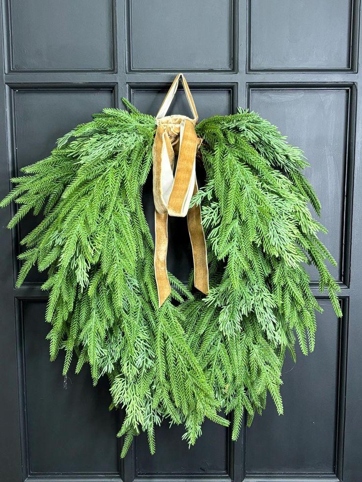 a wreath is hanging on the front door with a ribbon around it and some green leaves