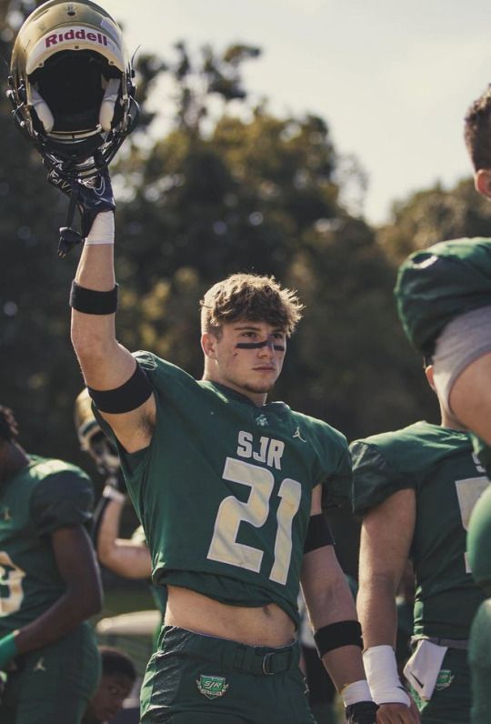 a football player is holding his helmet up in the air with other players behind him