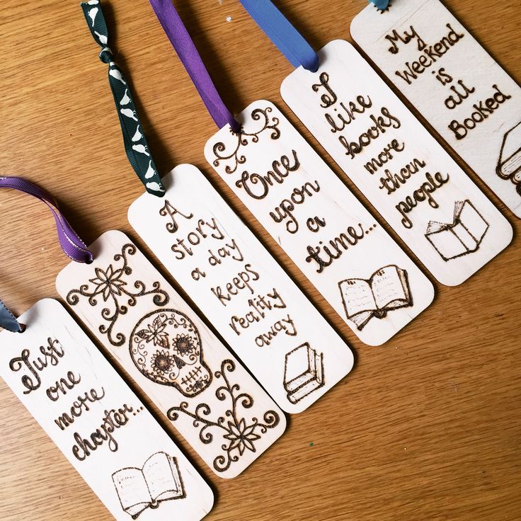 four bookmarks with writing on them sitting on a wooden table next to ribbon ties