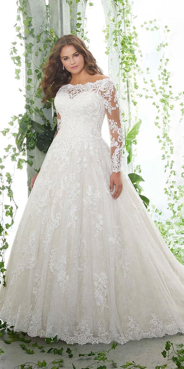 a woman in a white wedding dress posing for the camera with greenery behind her