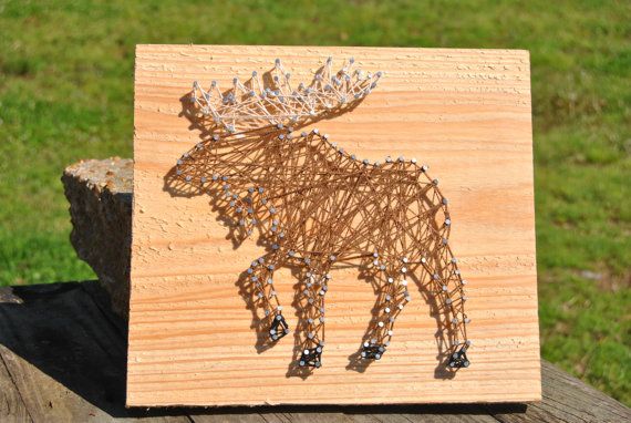 a string art moose is shown on a piece of wood with grass in the background