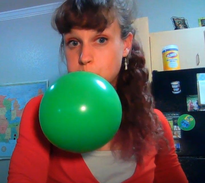 a woman holding a green balloon in her mouth