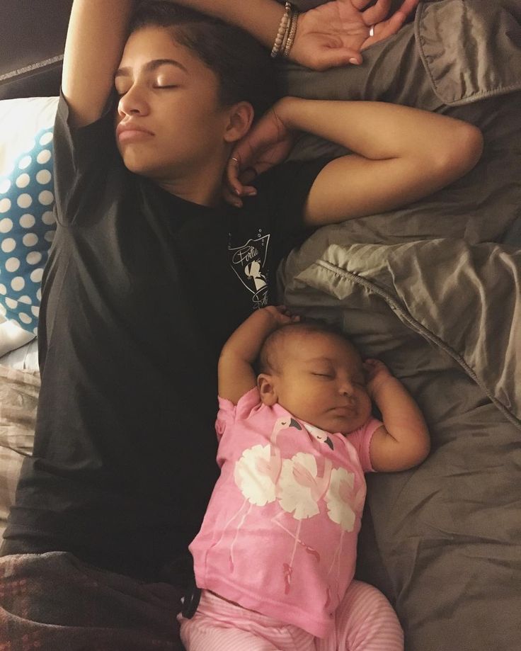 a woman laying on top of a bed next to a sleeping baby with her eyes closed