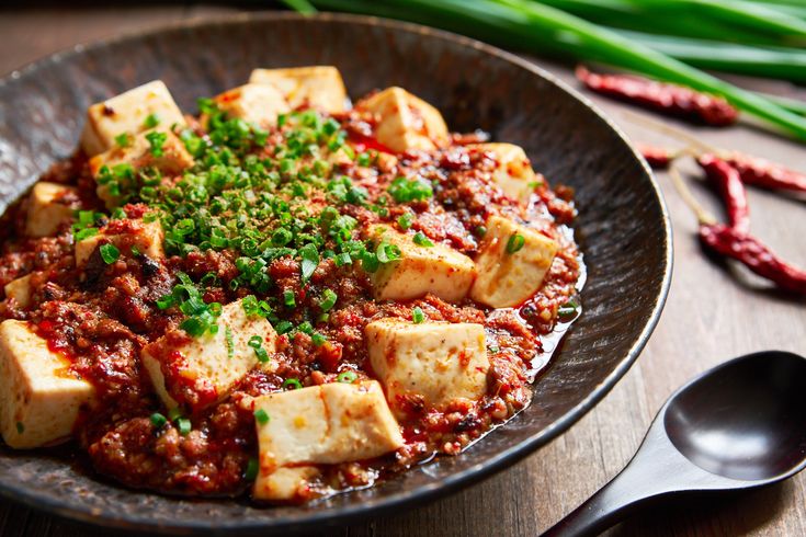 a plate with tofu and sauce on it next to some green onions in the background