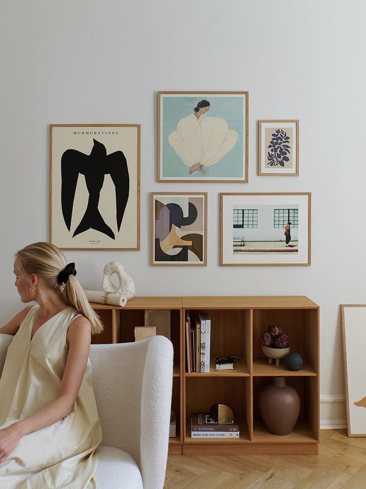 a woman sitting on a chair in front of a wall full of pictures and artwork