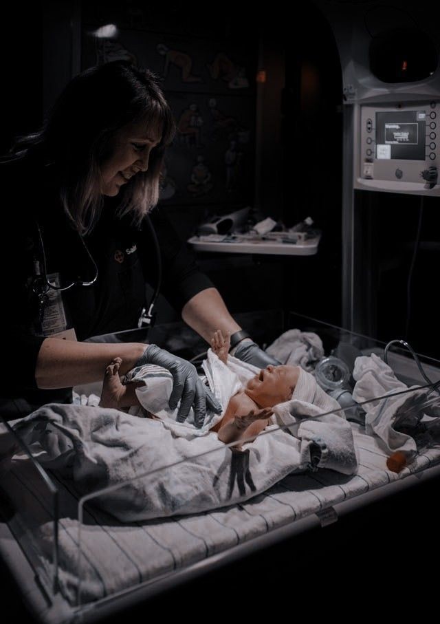 a woman holding a baby in a hospital bed with other medical equipment on the floor