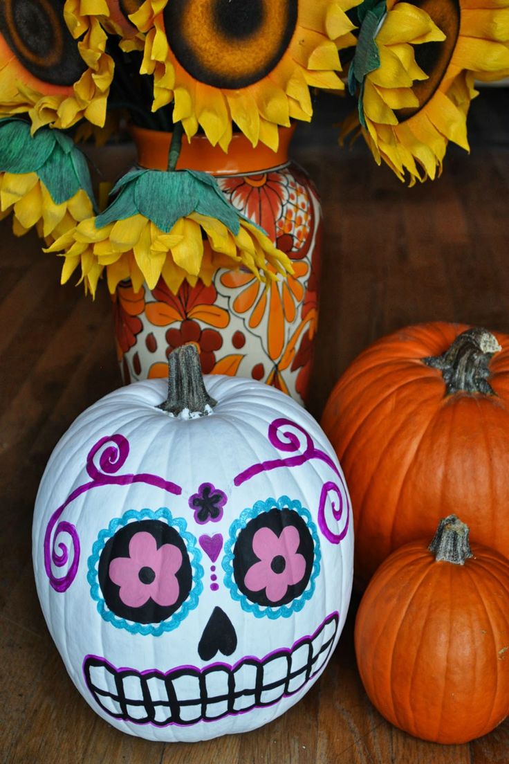 two pumpkins and a vase with flowers in it sitting on a wooden table next to each other