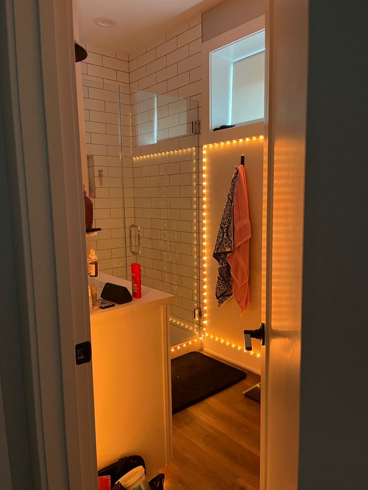 White polished bathroom with glass shower, with soft orange LED lights decorating the edges Cute Bathroom Lighting, Aesthetic Bathroom Shower Ideas, Aesthetic Bathroom Lights, Bathroom Couple Ideas, Mood Lighting For Bathroom, Bathroom Clean Aesthetic, Cute Apartment Ideas For Couples Bathroom, Cute Couples Apartment Ideas, Bathroom Decor Ideas Led Lights