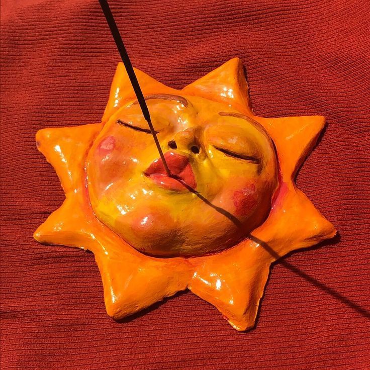 a ceramic sun with a face on it and two needles sticking out of the hole