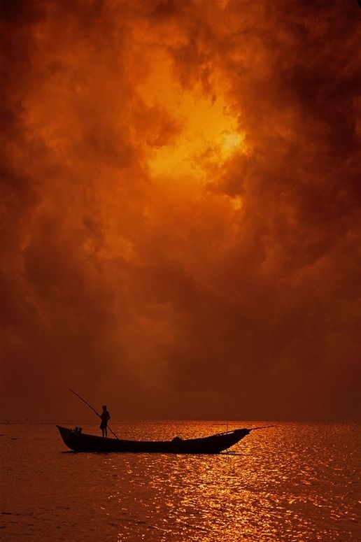 a man in a boat on the water under a cloudy sky